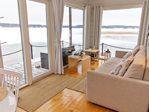 Una habitación acogedora con un sofá, una mesita y una silla. Cuenta con un ventanal con cortinas y vistas a un paisaje nevado.