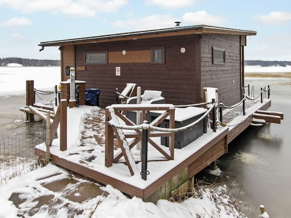 Una cabaña de madera con terraza, mobiliario exterior y vistas a un lago helado.