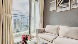 A modern living room with a beige sofa, a coffee table with a magazine, a vase with flowers, and a large window with a view of high-rise buildings. - Vinhomes Central Park-Premier Apartments (Ho Chi Minh City)