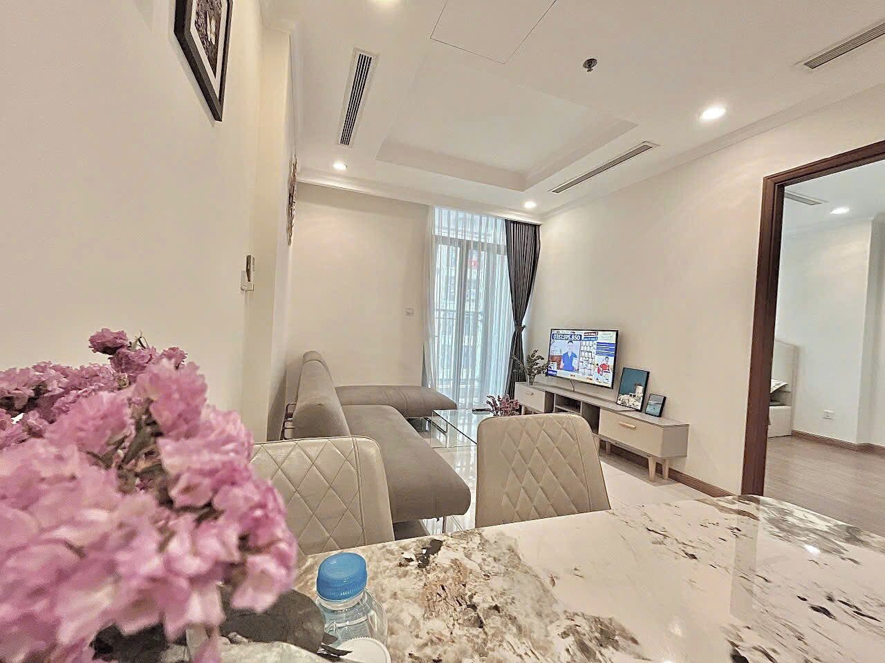 A modern living room with a sofa, a dining table with chairs, a TV, and a large window with curtains.