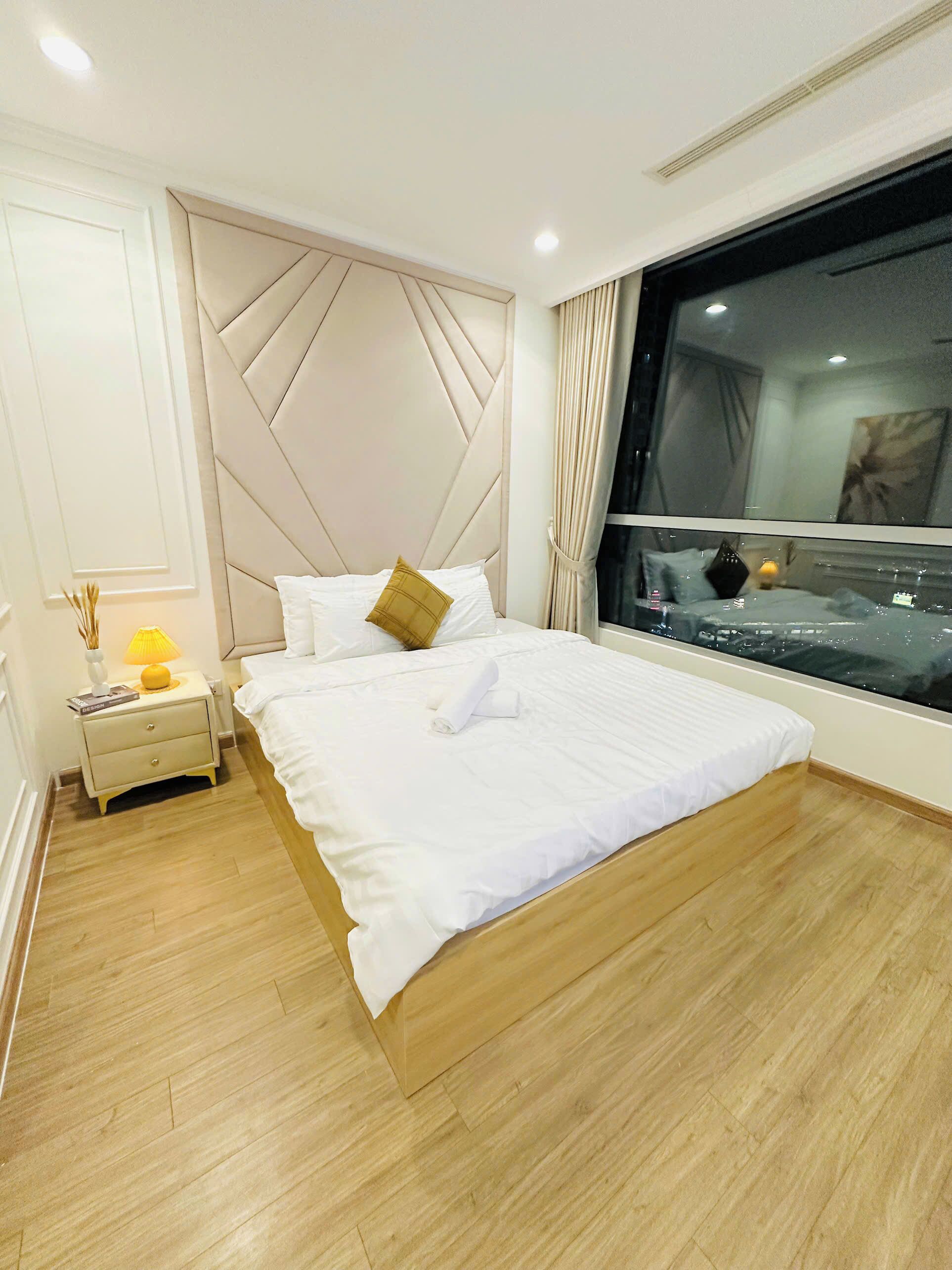 Une chambre moderne avec un grand lit, une table de chevet avec une lampe et une fenêtre donnant sur un beau paysage.
