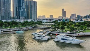 A marina with several yachts docked, surrounded by high-rise buildings and a park with trees. - Vinhomes Central Park-Premier Apartments (Ho Chi Minh City)