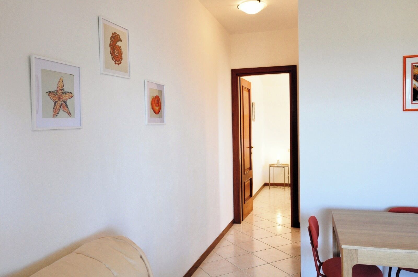A hallway with a dining area, featuring a table and chairs, and framed artwork on the walls.
