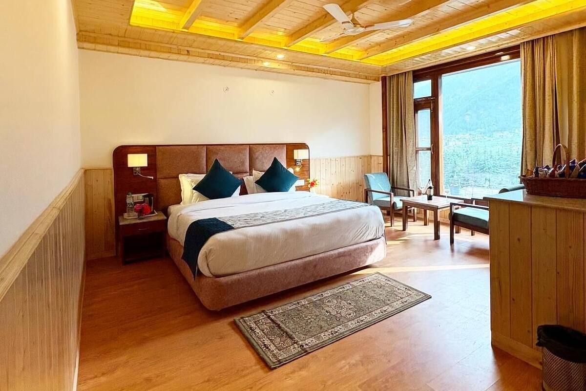 Een slaapkamer met een houten plafond, een groot bed, een bureau en uitzicht op het landschap.