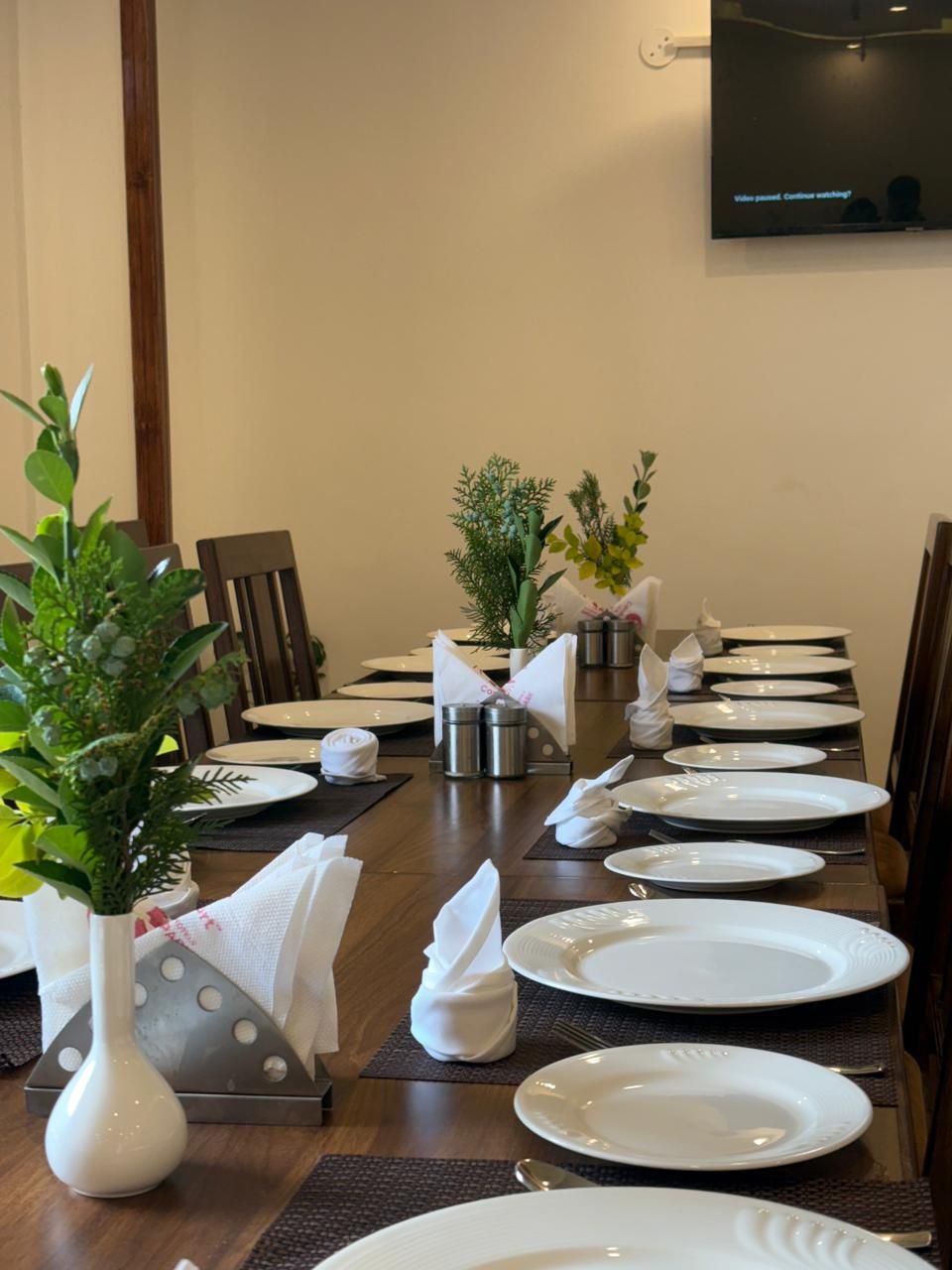 A dining table set for a meal with white plates, folded napkins, and small potted plants.