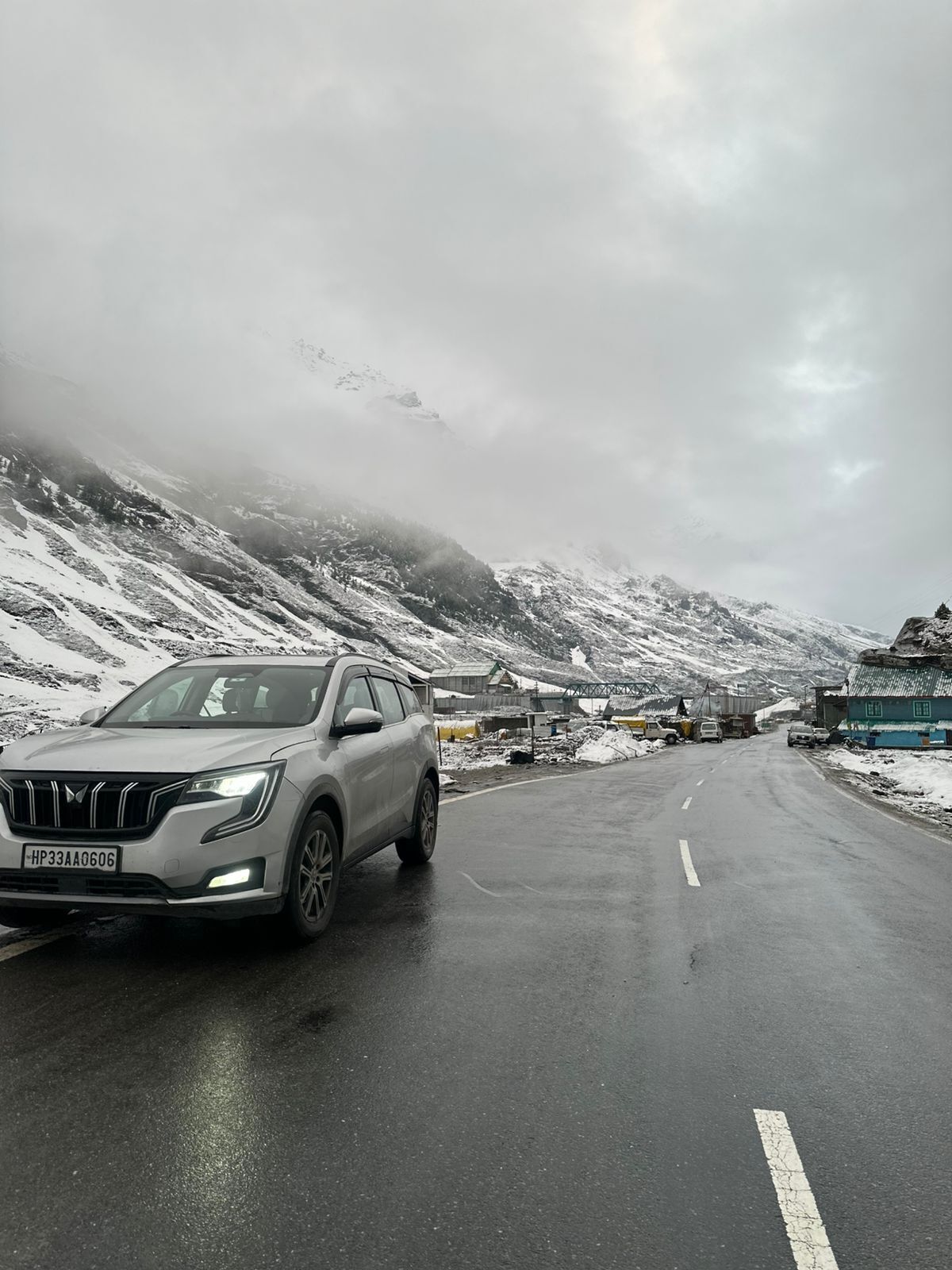 Un SUV blanco estacionado en una carretera con montañas nevadas al fondo.