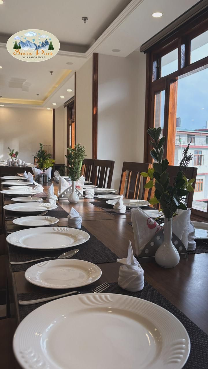 Un comedor con una larga mesa dispuesta para una comida, con platos blancos, servilletas y jarrones con plantas.