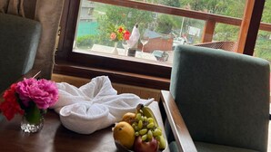 A room with a wooden table, a green chair, a window with a mountain view, and a bouquet of flowers. - Snow Park Villas & Resort Manali (Manali)