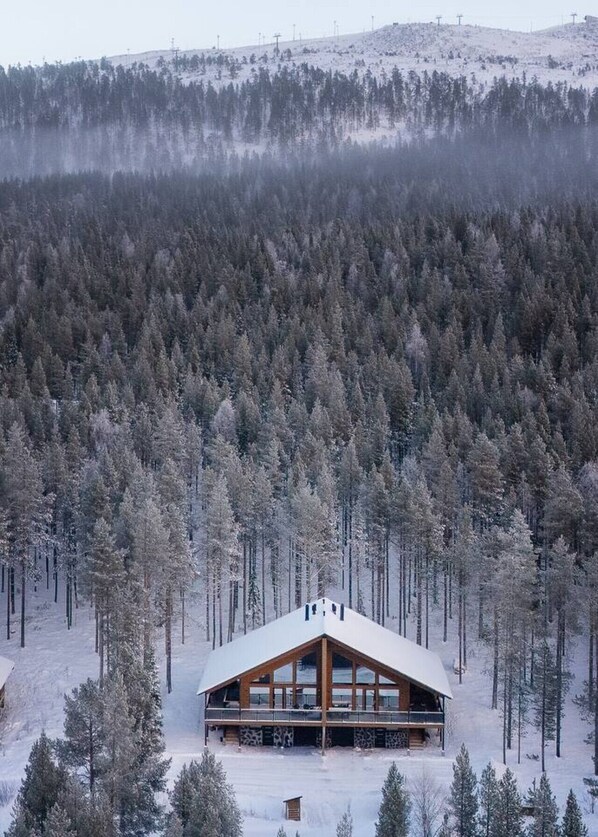 Una cabaña con una gran estructura de madera, rodeada por un bosque denso y terreno cubierto de nieve.