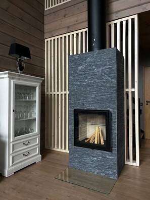 Een moderne woonkamer met een stenen open haard, een wit kastje met glazen deuren, en houten lamellen aan de muur.