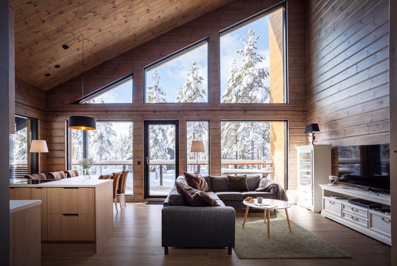 A modern interior with a kitchen, dining area, and living room, featuring large windows and wooden paneling.