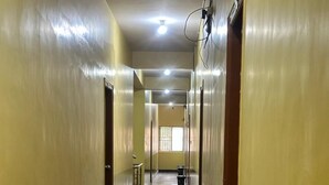 A long, narrow hallway with a shiny, reflective floor and yellow walls. There are doors on both sides, and a few trash bins are visible along the hallway. - Bms Luxury homes (Anekal)