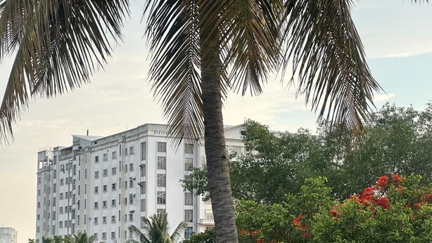 A multi-story building with a white facade and a blue fence in the foreground. - Bms Luxury homes (Anekal)