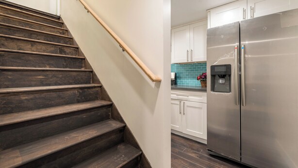 Una escalera conduce a una cocina con armarios blancos y un refrigerador de acero inoxidable.