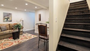 Una sala de estar con un sofá, una mesa de centro de vidrio, una silla, una alfombra y una escalera.