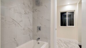 Un baño con pared de ducha de mármol, bañera y ventana con vistas.
