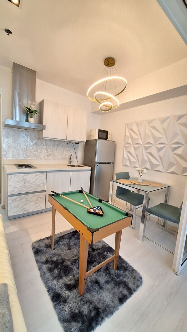 A compact kitchen with a pool table, a refrigerator, and a dining area with a modern chair and table.
