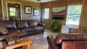 A cozy living room with a brown leather sofa, a wooden coffee table with speakers, and a large fern plant.