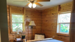 A wooden cabin bedroom with a bed, a nightstand, a lamp, and a ceiling fan.