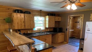 A kitchen with wooden cabinets, a central island with stools, a refrigerator, and a ceiling fan.