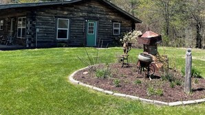 A rustic log cabin with a green door, surrounded by a well-maintained lawn and a garden with a bird bath and decorative rocks.