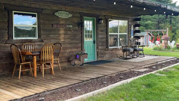 A rustic wooden building with a porch, a welcome sign, and a table with chairs.
