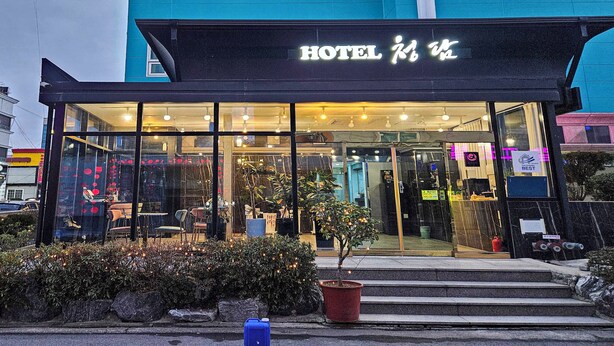 Een hotelgevel van glas, een bord en een kleine boom op de voorgrond.