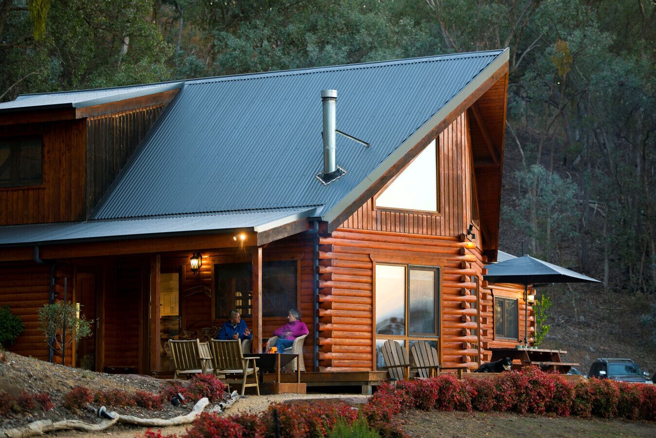 A log cabin with a porch, two chairs, a table, and a car parked outside.