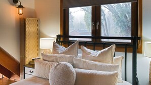 Un dormitorio con cama, almohadas, una mesita de noche, lámpara, ventana con vistas y una lámpara de pared.