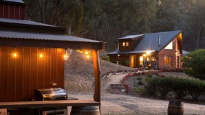 Una cabaña rústica con comedor, mobiliario exterior y un camino de grava que lleva a la entrada.