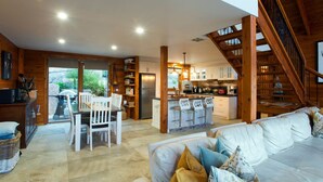 Amplia sala de estar con sofá, mesa de comedor con sillas, cocina con barra y una escalera.