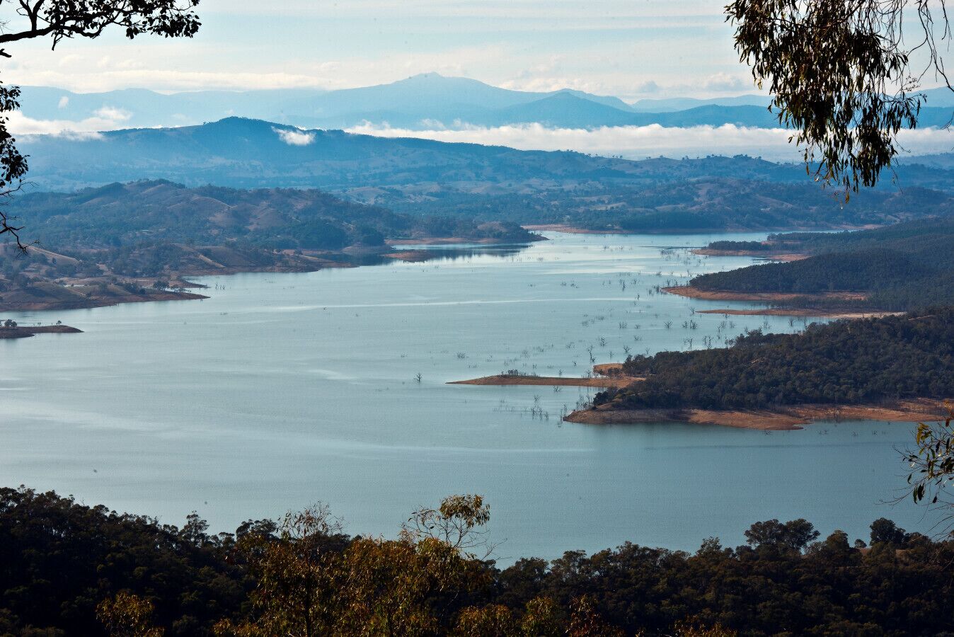A panoramic view of a large lake surrounded by hills and trees.
