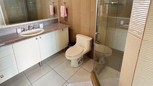 Ein modernes Badezimmer mit einer gläsernen Duschkabine, einer Toilette und einem Waschbecken mit Marmorplatte.