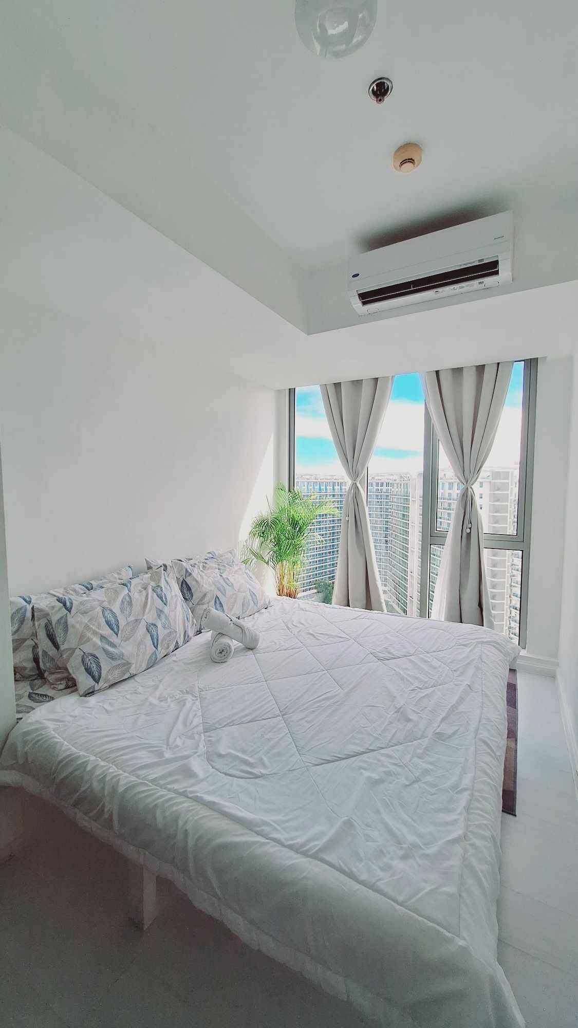 A modern bedroom with a large bed, an air conditioning unit, a potted plant, and a city view through the window.