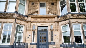 A building with a stone facade, a central entrance with a dark-colored door, and multiple windows. - Apartment in Harrogate Near Turkish Baths (Harrogate)