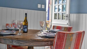 Una mesa de comedor dispuesta con platos, vasos y una botella de vino, rodeada de sillas a rayas.