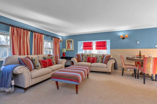 A living room with two sofas, a dining table, and a window with curtains.