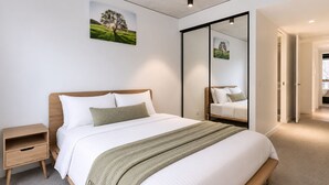 Een moderne slaapkamer met een groot bed, nachtkastjes, een spiegel en kunst aan de muur.