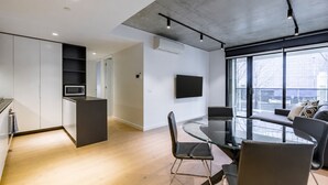Een moderne keuken met inbouwapparatuur, een eethoek met een glazen tafel en stoelen, en een groot raam met uitzicht op de stad.