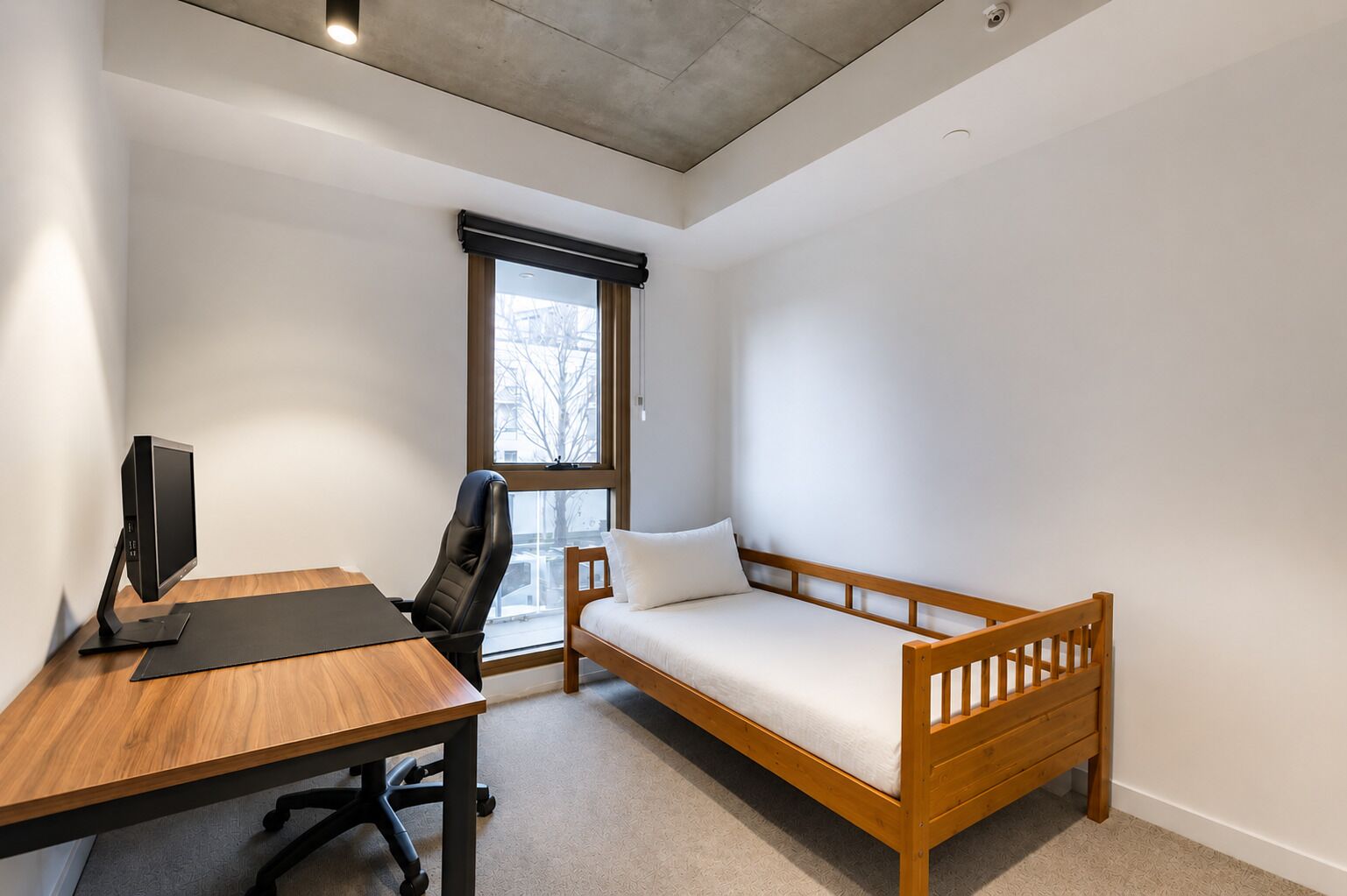 Una habitació amb escriptori, ordinador, cadira i llit de fusta.