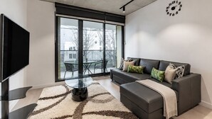 Een moderne woonkamer met een bank, een glazen salontafel, een flatscreen-tv en een groot raam.
