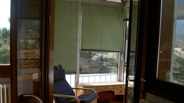 A room with a large window, a chair, a table, and a radiator.