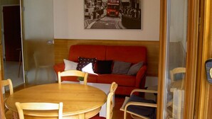 A living room with a red sofa, wooden dining table, and chairs. A vintage bus photo hangs on the wall.