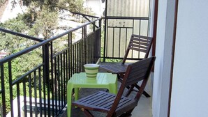 A balcony with a table and two chairs, a green plastic stool, and a metal railing.
