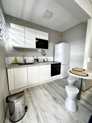 Una cucina compatta con mobili bianchi, un forno a microonde, una macchina da caffè e un frigorifero.