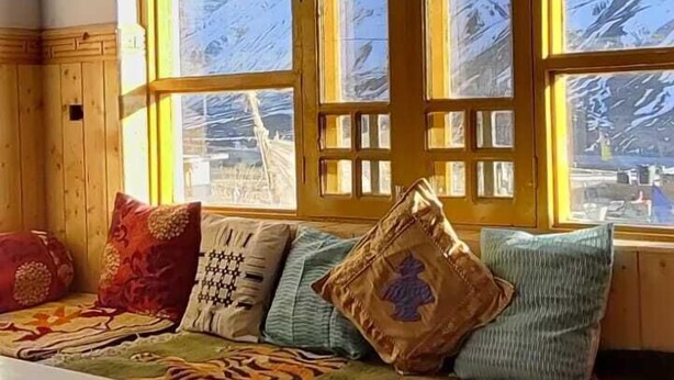 A room with a large window overlooking a snowy mountain. - Buddha Home Stay Kaza (Kaza)