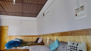 A room with a wooden ceiling, a bed with multiple pillows, a window with curtains, and a wall socket. - Buddha Home Stay Kaza (Kaza)