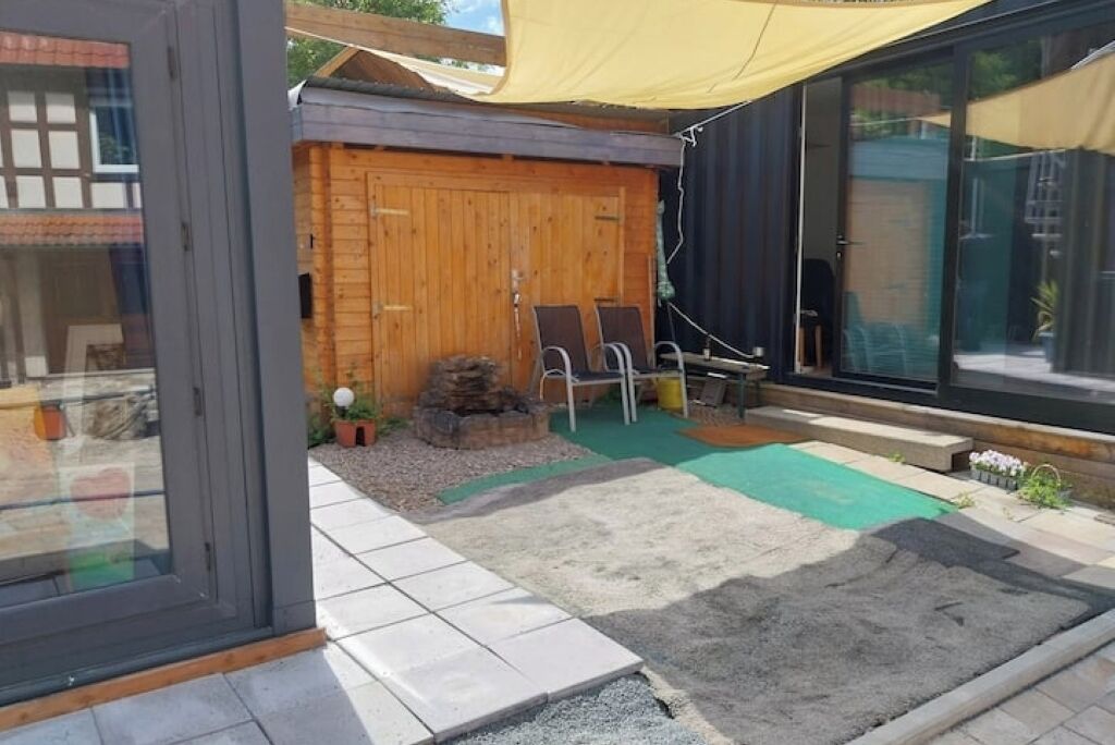 Un patio moderno al aire libre con terraza de madera, un tapete verde y una zona de estar con dos sillas.