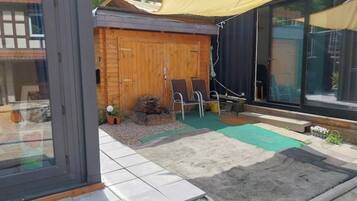 Un patio moderno al aire libre con terraza de madera, un tapete verde y una zona de estar con dos sillas.