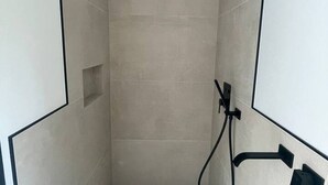 A narrow shower area with tiled walls and a black showerhead.